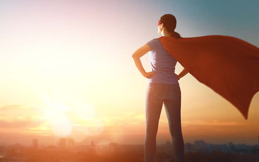 woman in superhero costume looking at sunrising from an elevated spot
