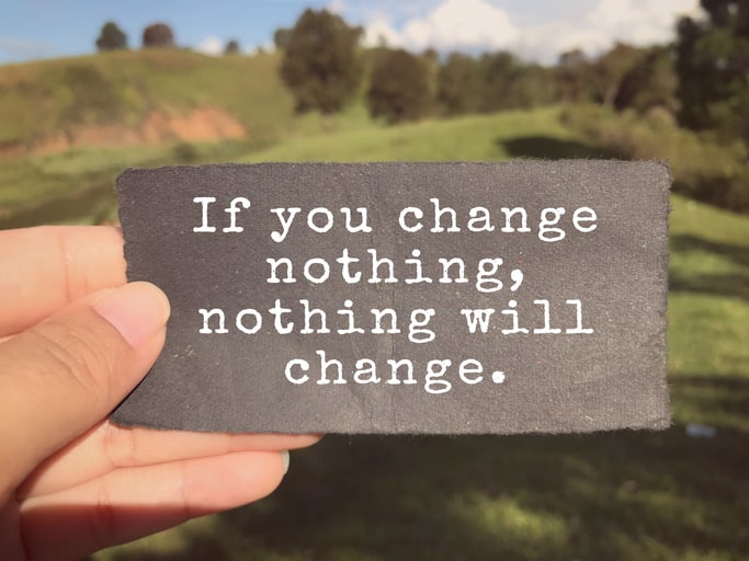 hand holding a sign over a green field that says if you change nothing. nothing will change.