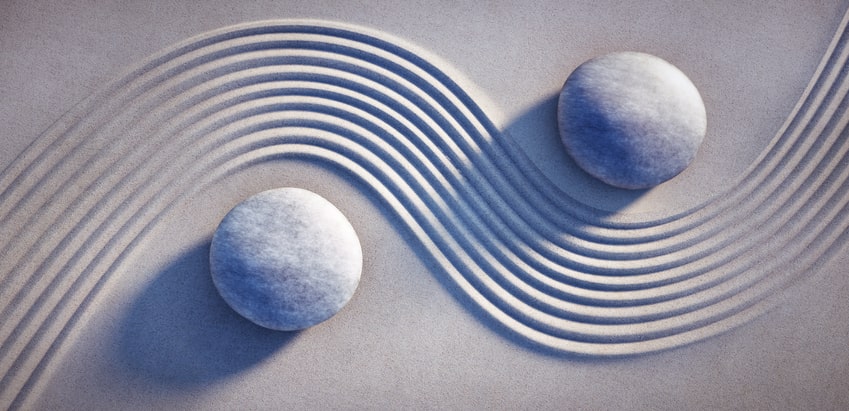 two stones in sand with a wave in between depicting sameness and balance