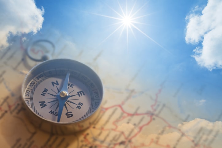 compass pointing true north on old map in cloud with sun